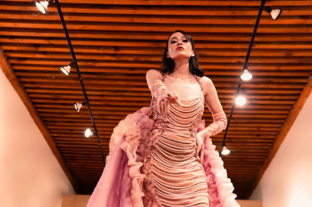 Como a Colcci construiu uma narrativa cosmopolita para o outono em Paris Modelo apresenta um vestido rosa em uma passarela de moda sob iluminação cênica.
