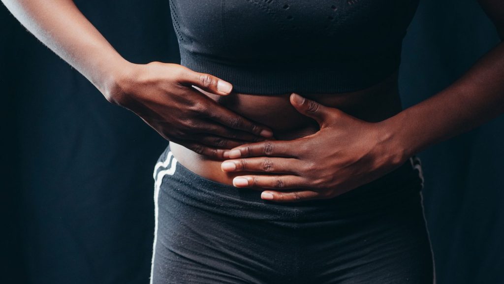 Doenças inflamatórias intestinais avançam no Brasil e exigem atenção Pessoa com as mãos sobre o abdômen, indicando desconforto ou dor abdominal.